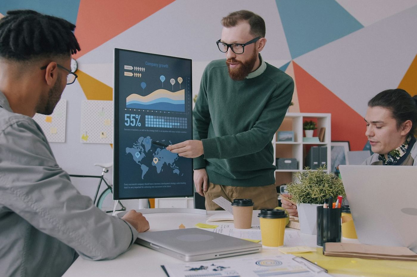 Three colleagues reviewing a growth chart on a large monitor in an office